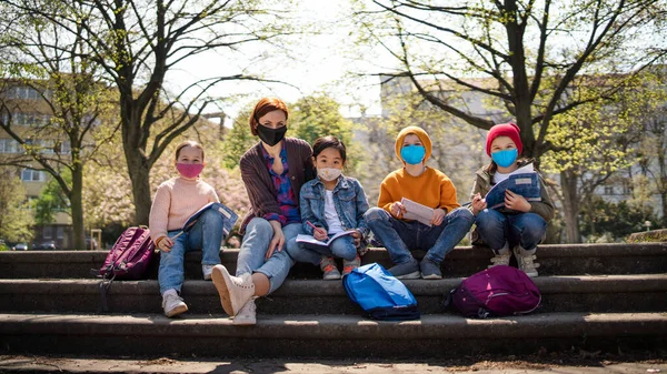 Insegnante con bambini piccoli seduti all'aperto nel parco cittadino, formazione di gruppo e concetto di coronavirus. — Foto Stock