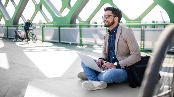 Junger Geschäftsmann pendelt mit dem Fahrrad auf dem Weg zur Arbeit im Freien in der Stadt mit dem Laptop. — Stockfoto