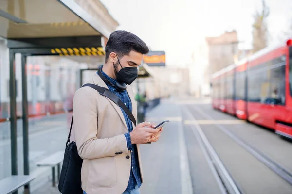 Mladý podnikatel dojíždějící s chytrým telefonem na cestě do práce venku ve městě, koronavirus koncept. — Stock fotografie