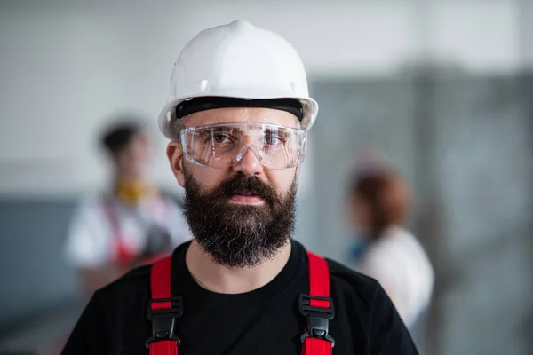 Ritratto di operaio con casco e occhiali protettivi all'interno in fabbrica guardando la macchina fotografica. — Foto Stock