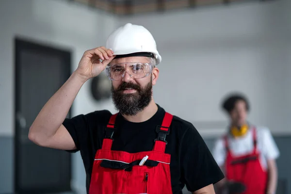 Portrét pracovníka s helmou a ochrannými brýlemi v továrně při pohledu do kamery. — Stock fotografie