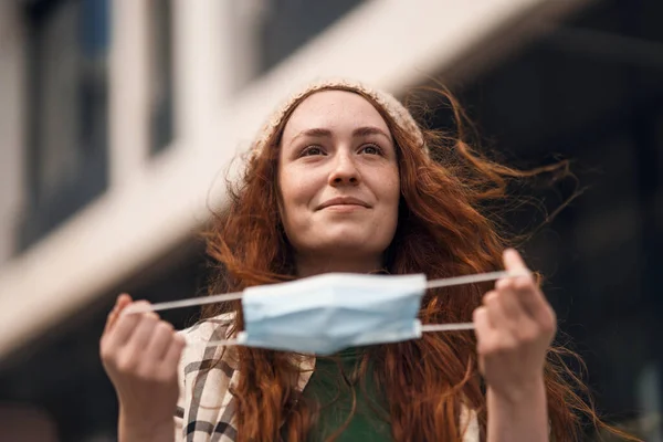 Retrato de una mujer joven quitándose la máscara facial al aire libre en la ciudad, vida después de la vacunación con covid-19. — Foto de Stock