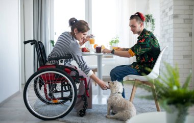 Evde oğlu ve köpeği olan tekerlekli sandalyede oturan sakat, olgun bir kadın yemek yiyor..