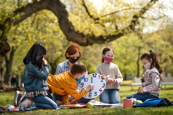 市内の公園で屋外に座っている小さな子供と教師,学習グループ教育とコロナウイルスの概念. — ストック写真