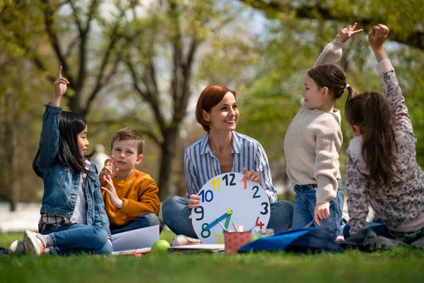 Lehrer mit kleinen Kindern sitzen draußen im Stadtpark, Lerngruppenpädagogik. — Stockfoto