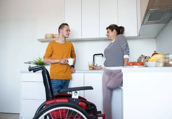 Tekerlekli sandalyedeki engelli kadın evde mutfakta arkadaşıyla konuşuyor.. — Stok fotoğraf