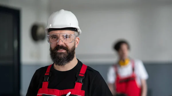 Retrato de trabalhador com capacete e óculos de proteção dentro de casa na fábrica olhando para a câmera. — Fotografia de Stock