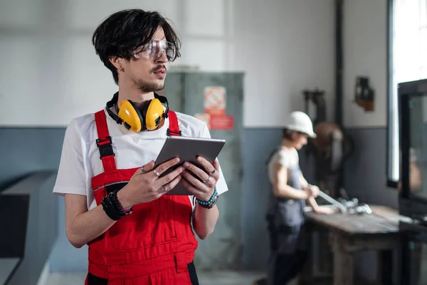 Portret młodego pracownika stojącego wewnątrz w fabryce patrzącego w kamerę. — Zdjęcie stockowe