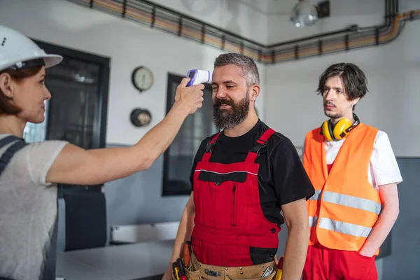 Grupo de trabajadores en interiores en fábrica, medición de temperatura y vuelta a la normalidad después de covid-19. — Foto de Stock