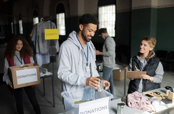 Grupp av volontärer som arbetar i välgörenhetsorganisationer donationscenter, sortera ut kläder och konserverad mat. — Stockfoto