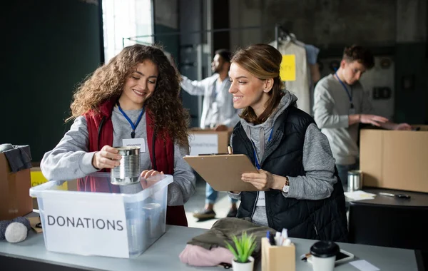 Grupp av volontärer som arbetar i välgörenhetsorganisationer donationscenter, sortera ut kläder och konserverad mat. — Stockfoto