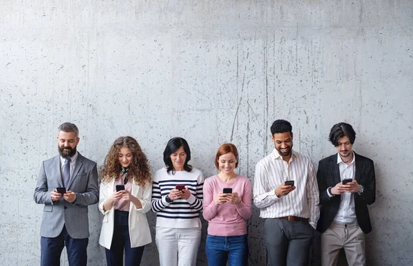 Портрет групи підприємців, що стоять на бетонній стіні в офісі, з використанням смартфона . — стокове фото