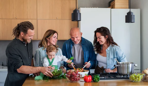 Glad flergenerationsfamilj inomhus tillagar grönsakssallad. — Stockfoto