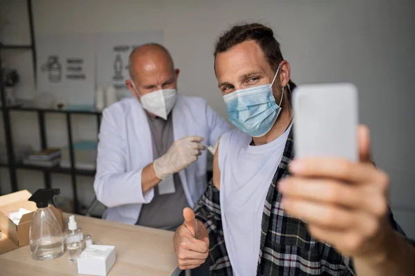 Happy mid adult man taking selfie when getting vaccinated, coronavirus concept. — Stock Photo, Image