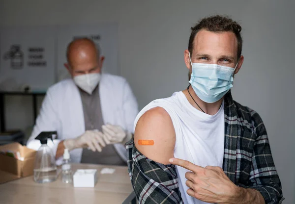 Buon uomo medio adulto dopo la vaccinazione covid-9, indicando intonaco sul braccio e guardando la fotocamera. — Foto Stock