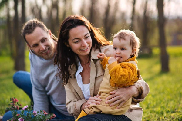 Gelukkig jonge ouders met kleine dochtertje zitten op gras in de natuur, ontspannen. — Stockfoto