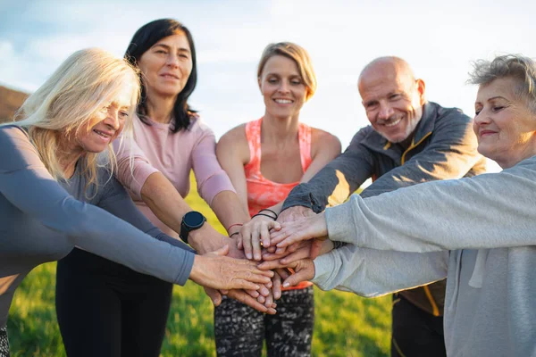 Skupina seniorů se sportovním instruktorem stohování rukou po cvičení venku v přírodě, aktivní životní styl. — Stock fotografie