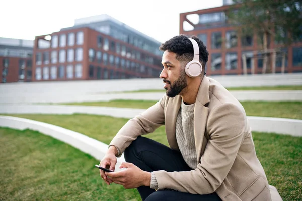 Homme avec casque et martphone à l'extérieur dans le parc en ville, se reposant. — Photo