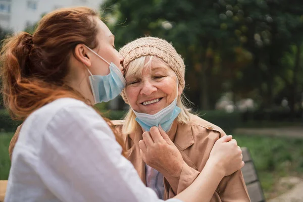 Portrait of young woman kissing grandmother outdoors in city, life after covid-19 vaccination. — Stock Photo, Image