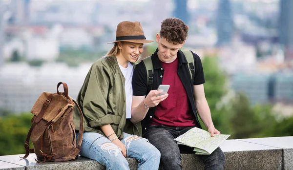 Jovens viajantes casal com mapa na cidade de férias, usando smartphone. — Fotografia de Stock