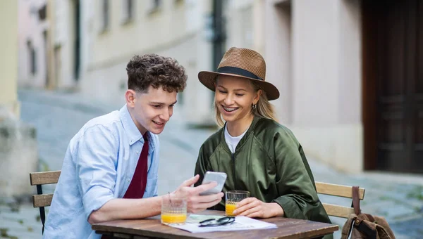 Unga par resenärer som använder smartphone i staden på semester, sitter i uteservering. — Stockfoto