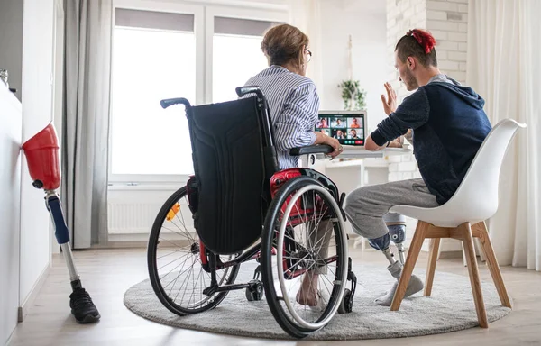 Widok z tyłu osób niepełnosprawnych siedzących przy stole w domu, koncepcja połączeń wideo. — Zdjęcie stockowe