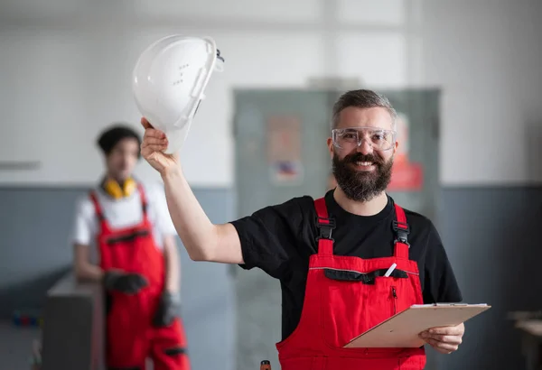 Portrait of cheerful worker with helmet and protective glasses indoors in factory looking at camera. — Stock Photo, Image