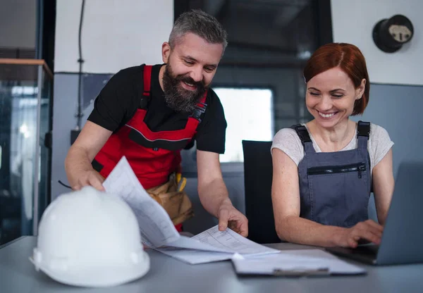 Férfi és női munkások vagy ipari mérnökök laptoppal a gyárban, kérdések megvitatása. — Stock Fotó