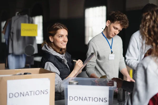 Grupo de voluntários que trabalham no centro comunitário de doação de caridade., triagem de roupas e alimentos enlatados. — Fotografia de Stock