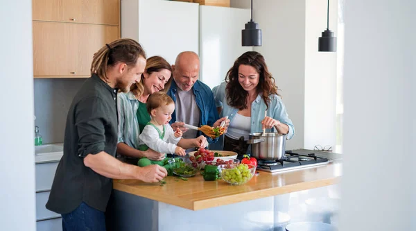 Glad flergenerationsfamilj inomhus tillagar grönsakssallad. — Stockfoto