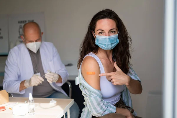 Glad ung kvinna efter covid-9 vaccination, pekar på gips på armen och tittar på kameran. — Stockfoto