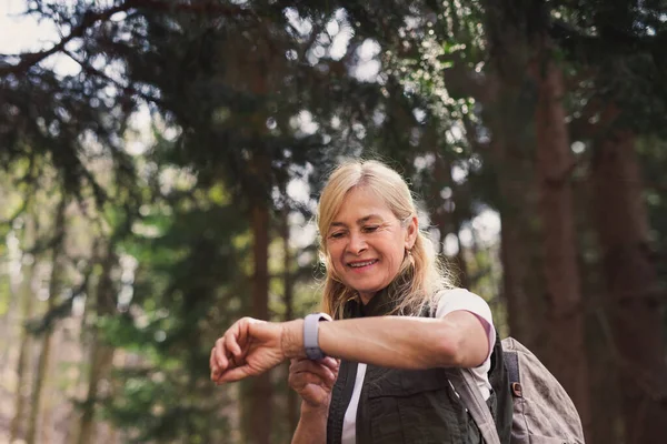 Senior žena pěší turistka venku procházky v lese v přírodě, pomocí Smartwatch. — Stock fotografie