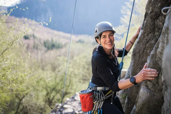 Senior kvinna klättra stenar och titta på kamera utomhus i naturen, aktiv livsstil. — Stockfoto