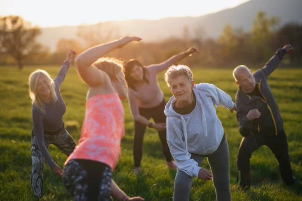 Seniorengruppe mit Sportlehrer bei Sonnenuntergang in der Natur, aktiver Lebensstil. — Stockfoto