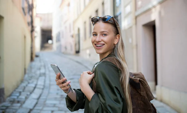 Jonge vrouw reiziger in de stad op vakantie met behulp van smartphone, op zoek naar camera. — Stockfoto