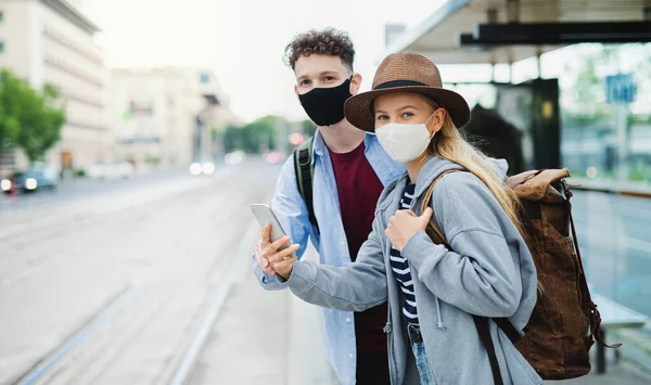 Young couple tourist travelers with smartphone on holiday at the bus stop in city, coronavirus concept. — Stock Photo, Image