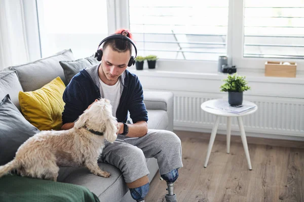 Portrait of disabled young man playing with dog indoors at home, leg prosthetic concept. — Stock Photo, Image