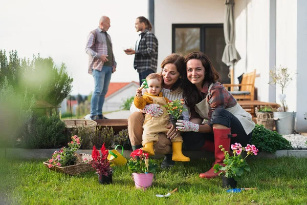 Happy multigeneration family outdoors planting flowers in garden at home, gardening concept. — Stok Foto