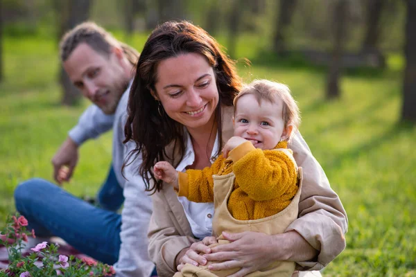 Padres jóvenes felices con hija pequeña sentada en la hierba en la naturaleza, relajante. — Foto de Stock