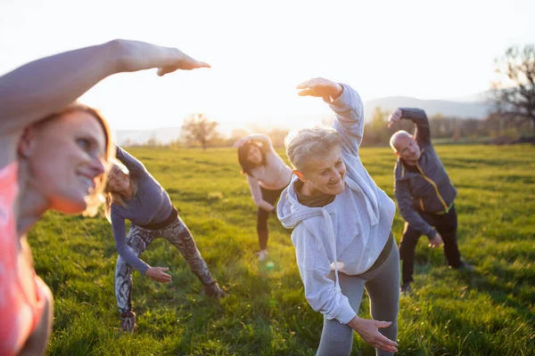Ομάδα ηλικιωμένων με εκπαιδευτή αθλητισμού κάνει άσκηση σε εξωτερικούς χώρους στη φύση κατά το ηλιοβασίλεμα, ενεργό τρόπο ζωής. — Φωτογραφία Αρχείου