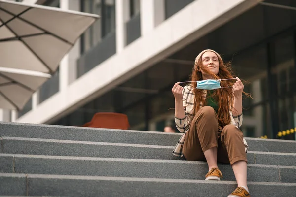 Retrato de una mujer joven quitándose la máscara facial al aire libre en la ciudad, vida después de la vacunación con covid-19. — Foto de Stock