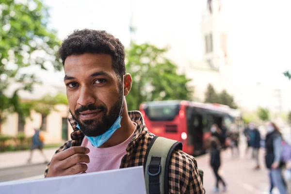 Retrato de un joven feliz quitándose la máscara facial al aire libre en la ciudad, concepto covid-19. — Foto de Stock