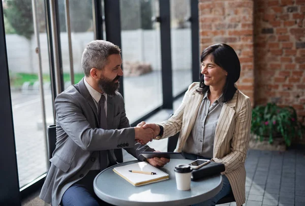 Porträt von Geschäftsleuten, die am Tisch sitzen und drinnen arbeiten und sich die Hände schütteln. — Stockfoto