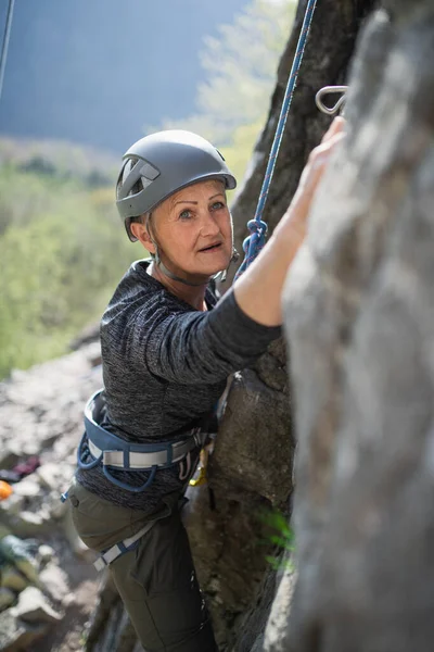 Senior kvinna klättra stenar och titta på kamera utomhus i naturen, aktiv livsstil. — Stockfoto