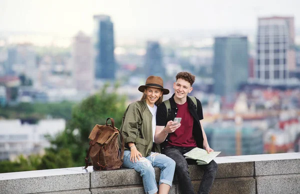 Jóvenes viajeros en pareja con mapa en la ciudad de vacaciones, utilizando el teléfono inteligente. — Foto de Stock