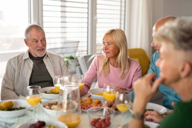 Bir grup kıdemli arkadaş içeride parti veriyor, masada yemek yerken konuşuyorlar..