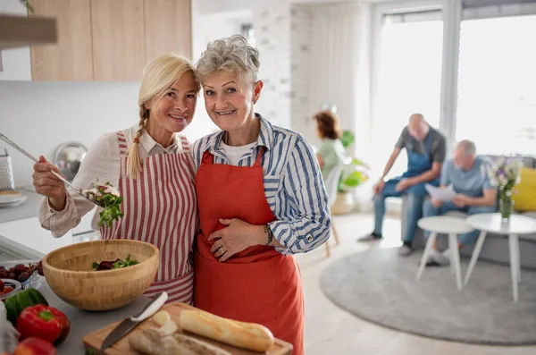 Grupp bestående av äldre vänner som festar inomhus, lagar mat och tittar på kameran. — Stockfoto