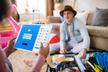 Unrecognizable couple with tablet planning holiday, booking flight.