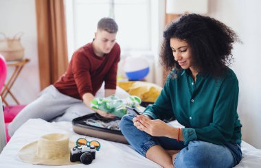 Happy young couple preparing and packing for summer holiday at home.