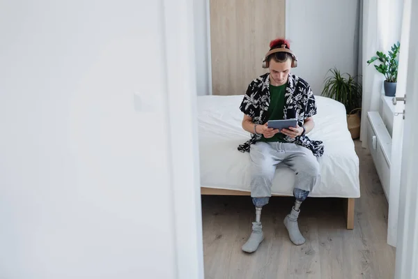 Retrato de jovem deficiente usando tablet na cama dentro de casa, conceito de prótese de perna. — Fotografia de Stock